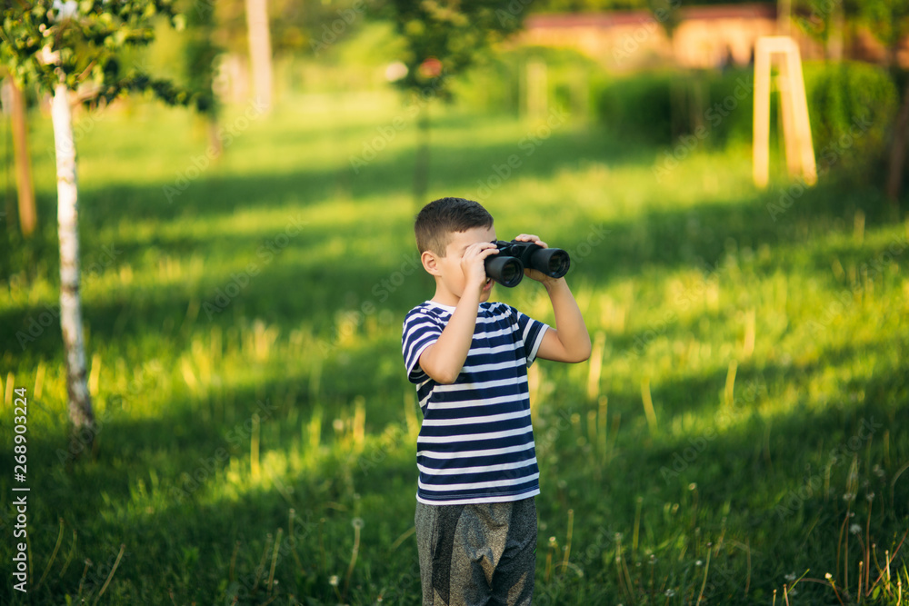 Little boy in a striped t-shirt looks through binoculars .Spring, sunny weather Little boy in a striped t-shirt looks through binoculars .Spring, sunny weather