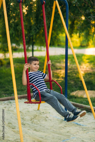A little boy in a striped T-shirt is playing on the playground, Swing on a swing