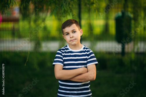 A little boy in a striped T-shirt standing in front of green background. Smiling and looking to the photographer