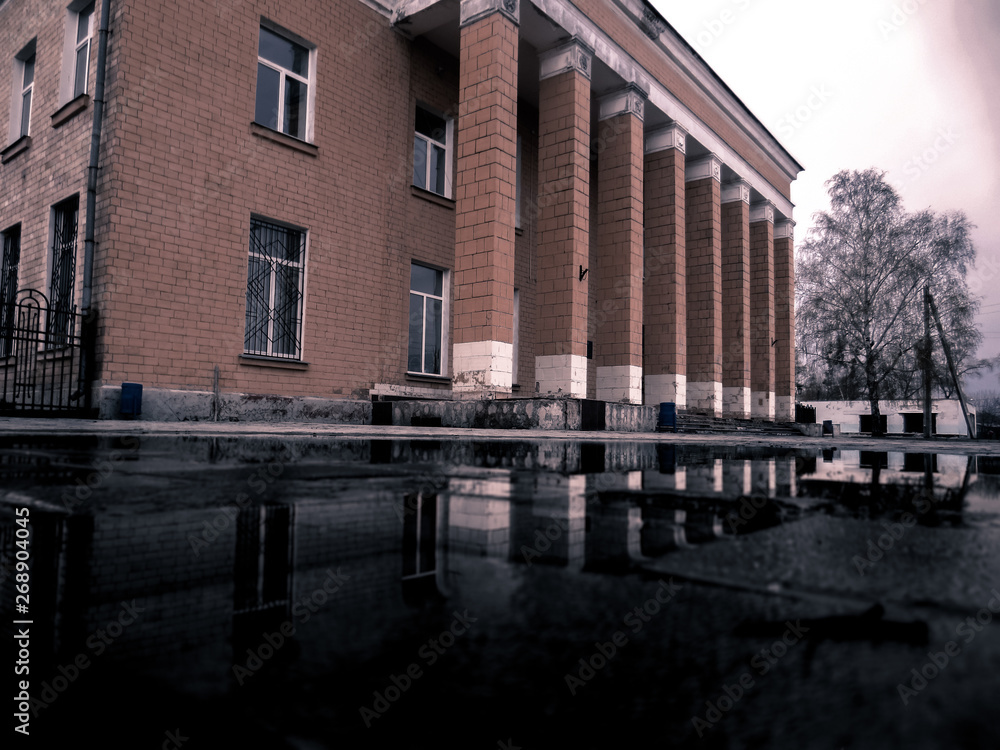 Old brown building with columns. A building with columns is reflected on the wet ground