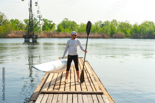 Man carrying kayak and oar after water sports at warm weather