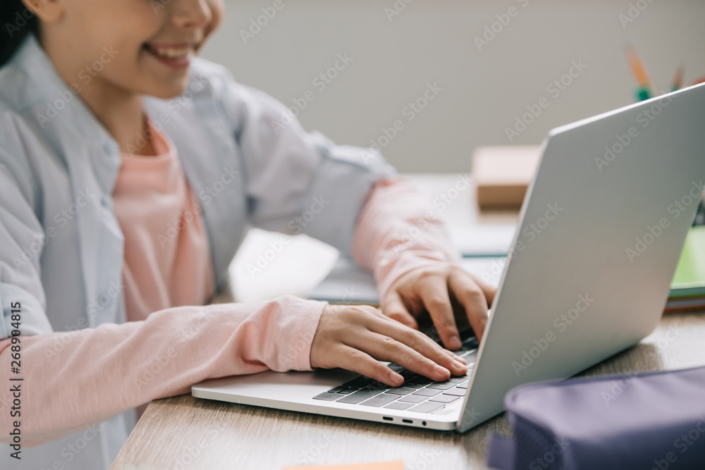 partial view of smiling schoolkid using laptop while doing schoolwork at home partial view of smiling schoolkid using laptop while doing schoolwork at home