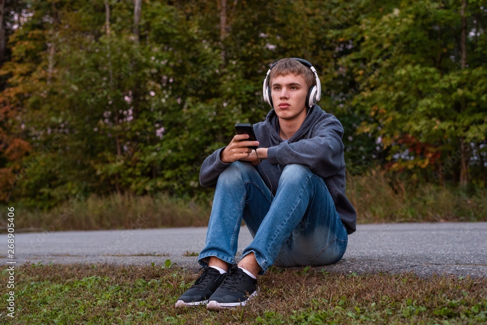 Upset teenager sitting on the ground all alone while listening to some music. Upset teenager sitting on the ground all alone while listening to some music.