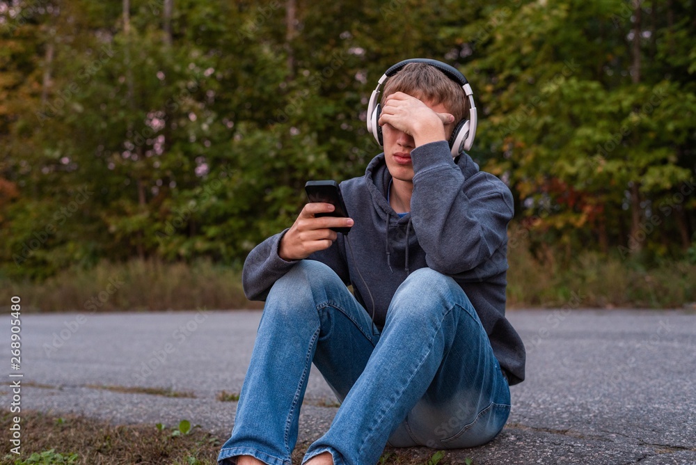 Upset teenager sitting on the ground all alone while listening to some music. Upset teenager sitting on the ground all alone while listening to some music.