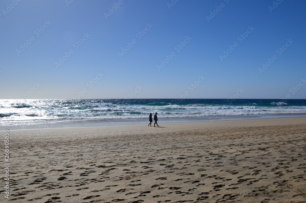 Morro Jable, Fuereventura, Spain. An unidentified couple walking along the coastline. Jandia Playa beach on a sunny, windy day. 