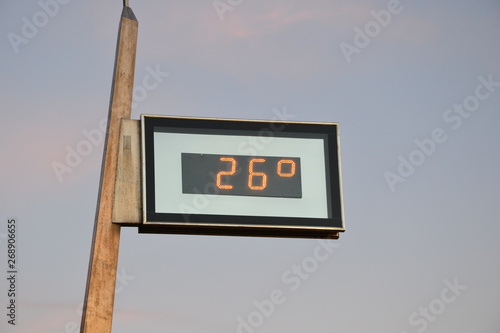 Outdoor thermometer indicating the high temperature - 26 degrees. Sky before sunset with slightly pink clouds in the background 