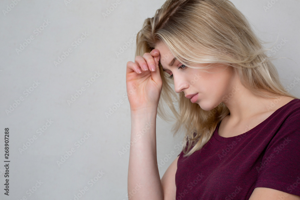 Tired blonde girl standing near the grey wall. Space for text Tired blonde girl standing near the grey wall. Space for text