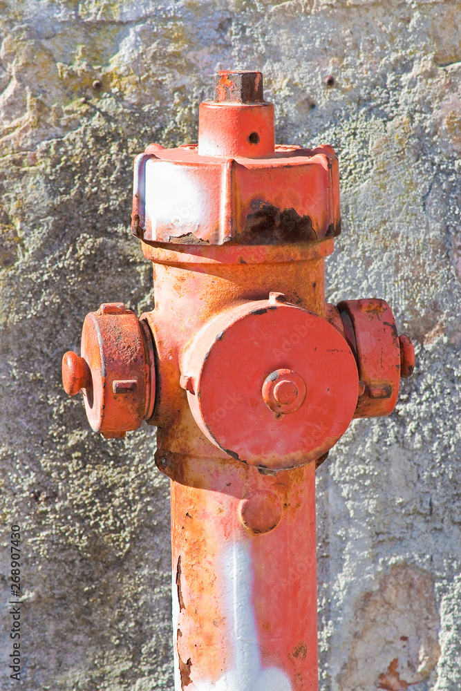 Old rusty red hydrant against a damaged plaster wall Old rusty red hydrant against a damaged plaster wall