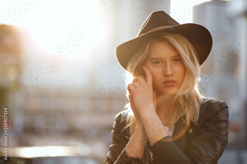 Pretty blonde woman wearing black hat posing with warm sun light. Empty space