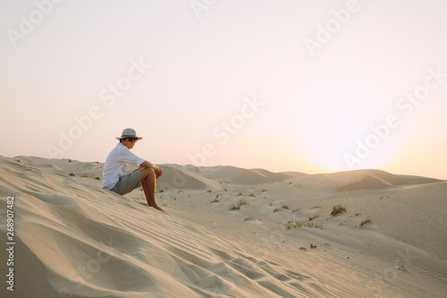 Man sitting on a dune in the desert while watching the sunset