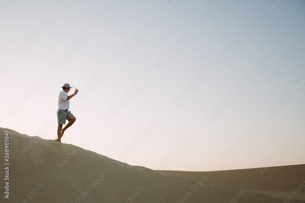 Young man walking on dunes in the desert in Dubai during the sunset Young man walking on dunes in the desert in Dubai during the sunset