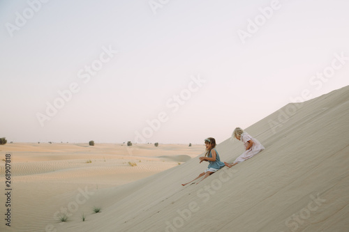 Two little girls sliding down the sand dune in Dubai