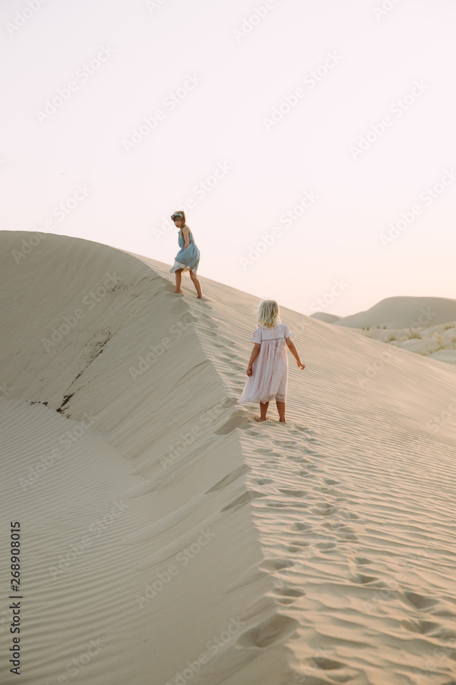 Fototapeta premium Two little girl walking on sand dunes in the desert in Dubai