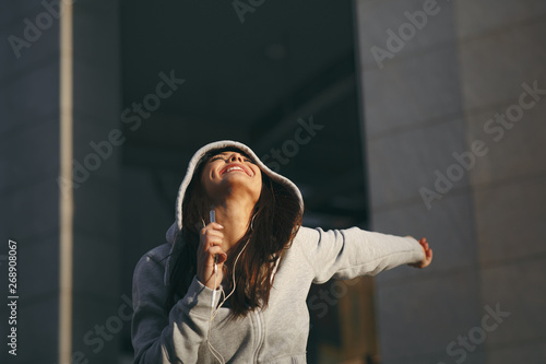 Young woman in gray hoodie enjoys music via headphones on the street