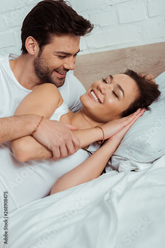 cheerful man looking at happy girl lying on bed with closed eyes
