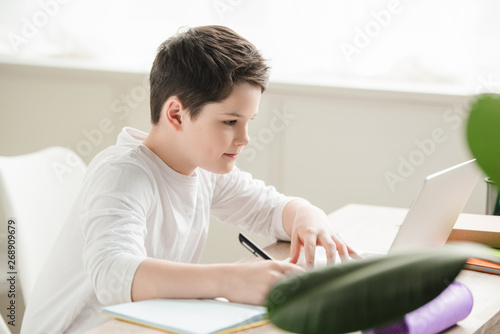 attentive writing in notebook and using laptop while doing schoolwork at home