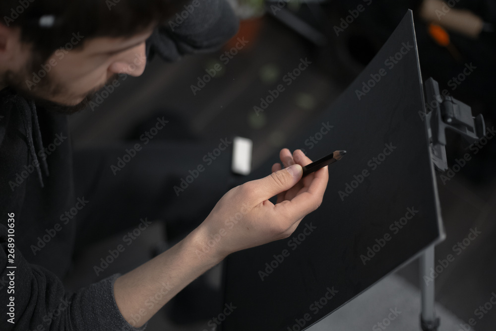 Close-up of young man painting with pencil on easel Close-up of young man painting with pencil on easel