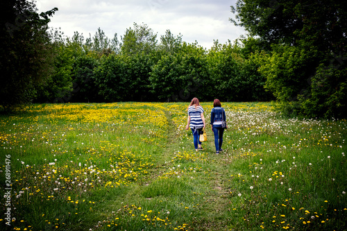 Two young woman on green and yellow dandelions field in the spring park.