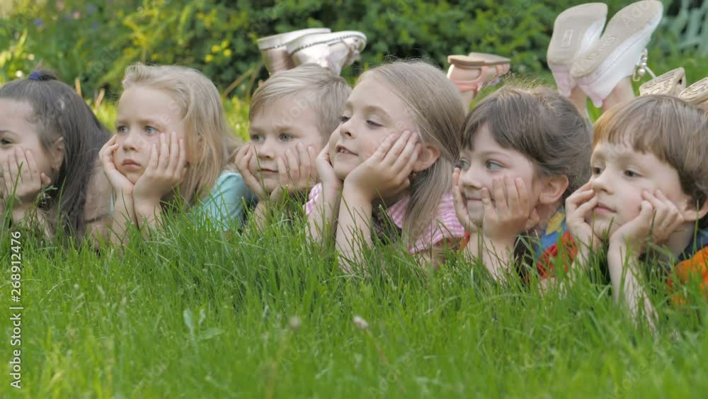Group of happy children lying on green grass outdoors in spring park Group of happy children lying on green grass outdoors in spring park