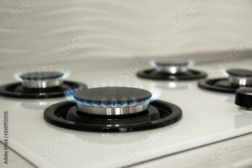 Gas burners with blue flame on modern stove, closeup. Space for text