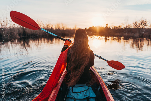 Canvas Print Back view of happy cute girl holding paddle in a kayak on the river