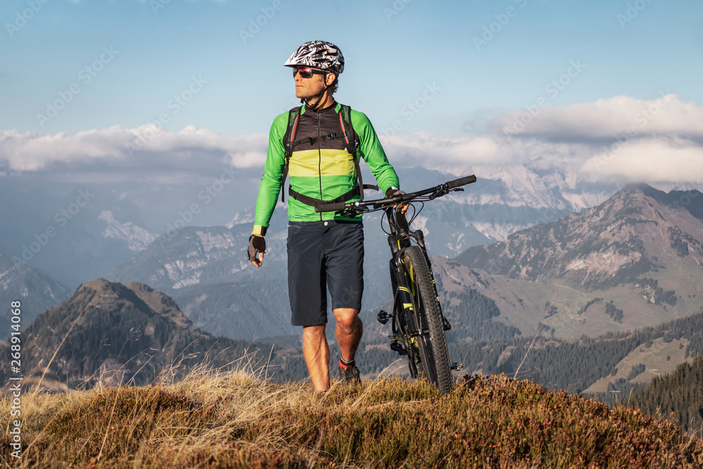 Male mountainbiker walking with his bike on a trail in the mountains