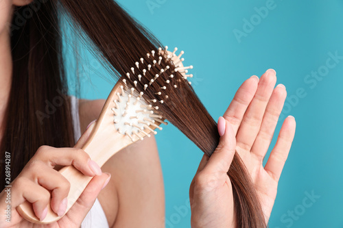 Woman with hair brush on color background, closeup