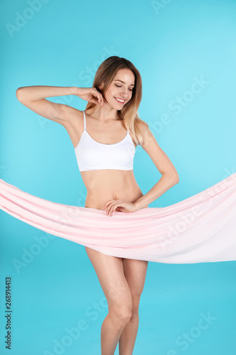 Young slim woman covering her body with fabric on color background