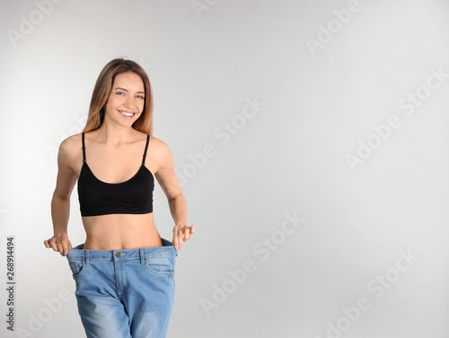 Slim woman in oversized jeans on light background, space for text. Perfect body