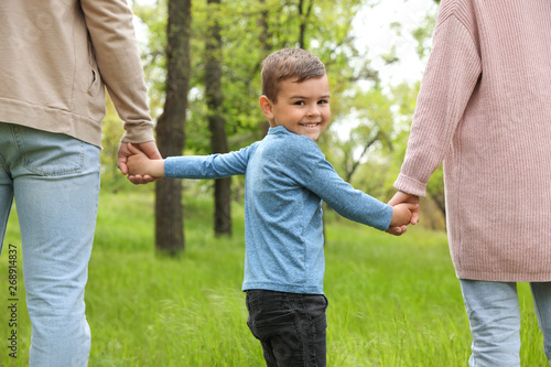 Happy little child holding hands with his parents in park. Family weekend photo