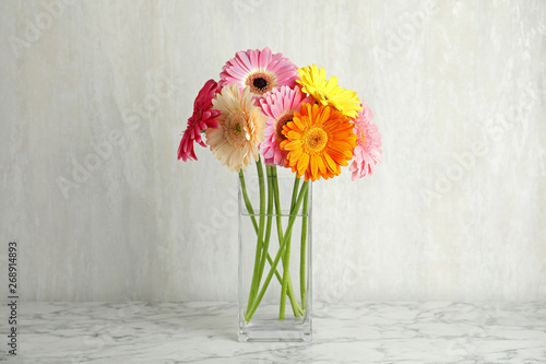 Bouquet of beautiful bright gerbera flowers in vase on marble table against light background