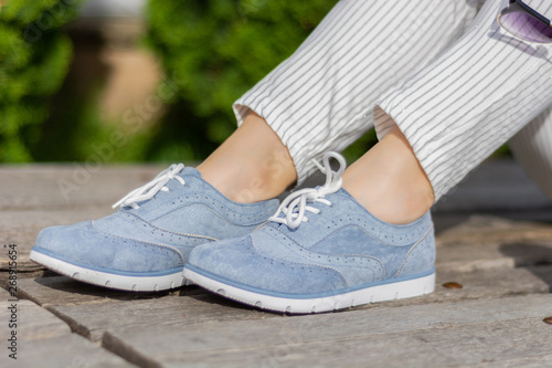 Modern woman legs with blue sneakers on a wooden bench in the park on a spring day. A girl wears striped pants and little bare skin around the legs wrists. Close up, selective focus