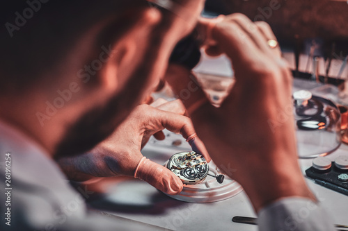 Mature clockmaster is fixing old watch for a customer at his busy repairing workshop. photo