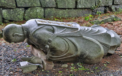 Dropped down, fallen buddhist monk granite stone statuesque in a Temple in Japan. Higo Honmyo Temple, Kumamoto Prefecture, Japan, Asia.