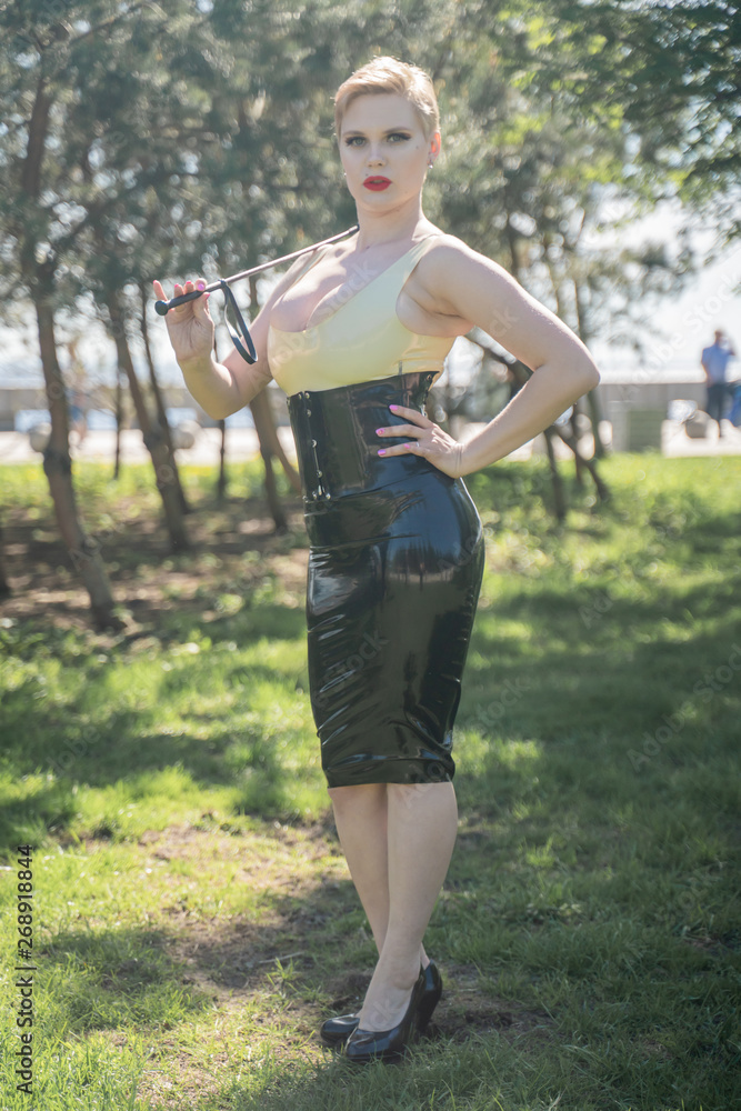 hot curvy woman with short hair and big boobs wearing latex kinky secretary  dress with feitsh corset and walking in the park alone Stock Photo | Adobe  Stock