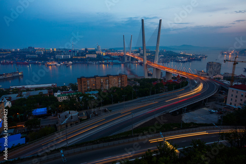 Golden cable-stayed bridge road car traffic from above. Modern Vladivostok Russia night illumination. Old and modern central buildings.
