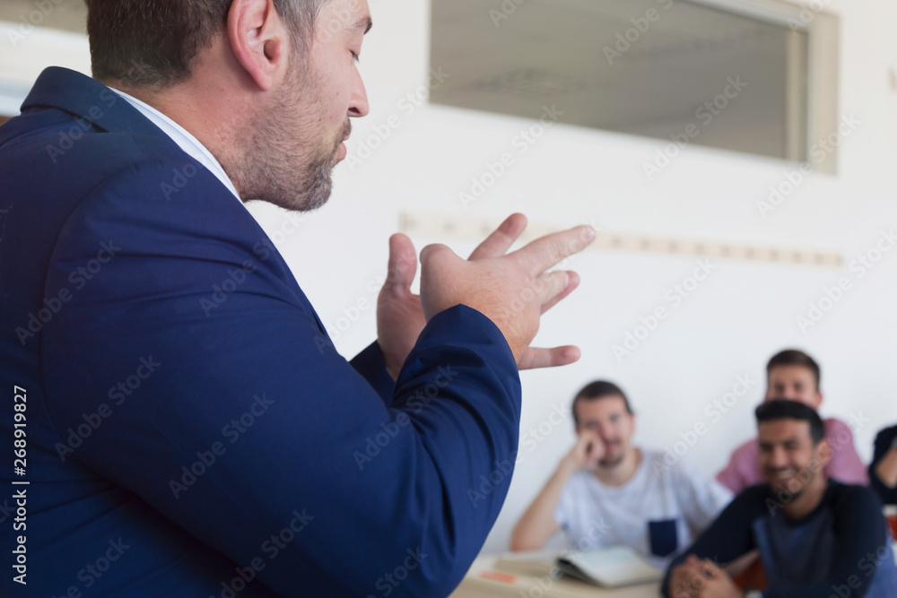 Fototapeta premium Male professor explain lesson to students and interact with them in the classroom.Helping a students during class. University student being helped by male lecturer during class.
