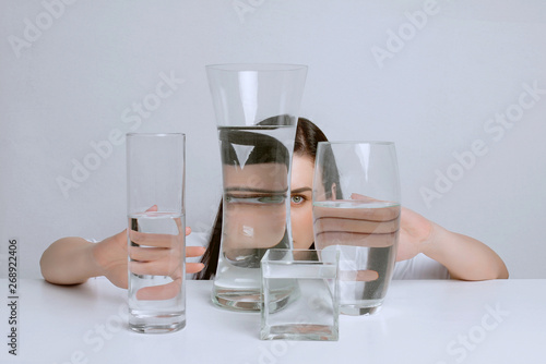 Art portrait of young attractive woman. Distorted reflection in glass vases with water.