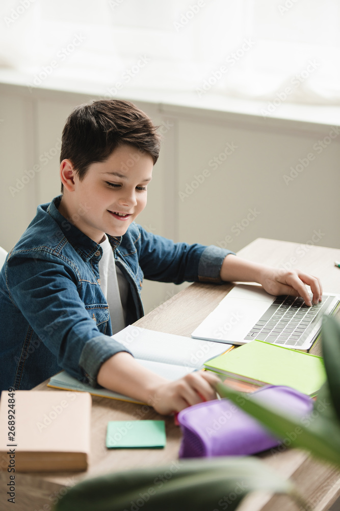 cheerful boy using laptop while doing schoolwork at home cheerful boy using laptop while doing schoolwork at home