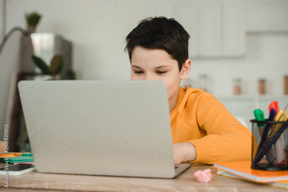 cute schoolkid using laptop while doing schoolwork at home cute schoolkid using laptop while doing schoolwork at home