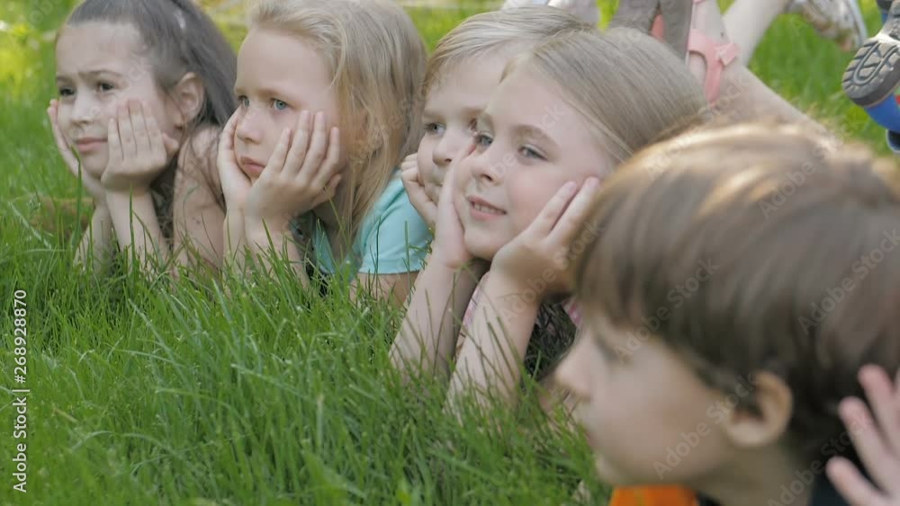 Group of happy children lying on green grass outdoors in spring park Group of happy children lying on green grass outdoors in spring park