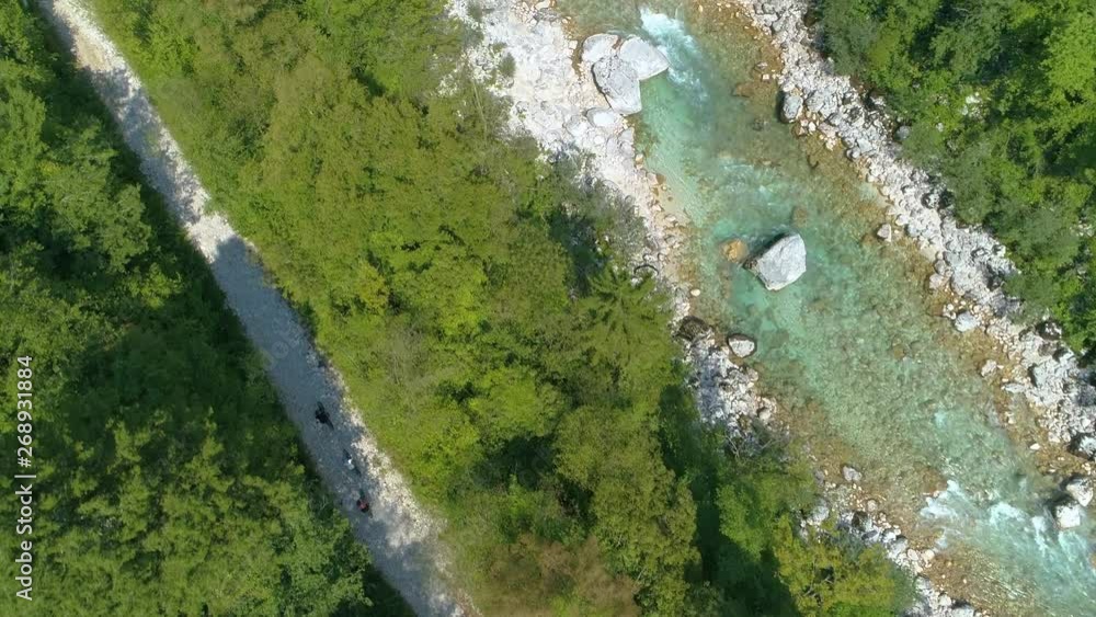 TOP DOWN: Flying above emerald Soca river as young bikers ride down the empty rocky path leading through the green forest. Tourists ride bicycles along scenic trail and colorful stream on sunny day. TOP DOWN: Flying above emerald Soca river as young bikers ride down the empty rocky path leading through the green forest. Tourists ride bicycles along scenic trail and colorful stream on sunny day.