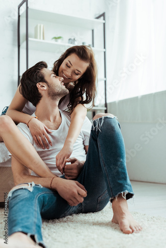 handsome man sitting on carpet and holding hands with cheerful girl at home