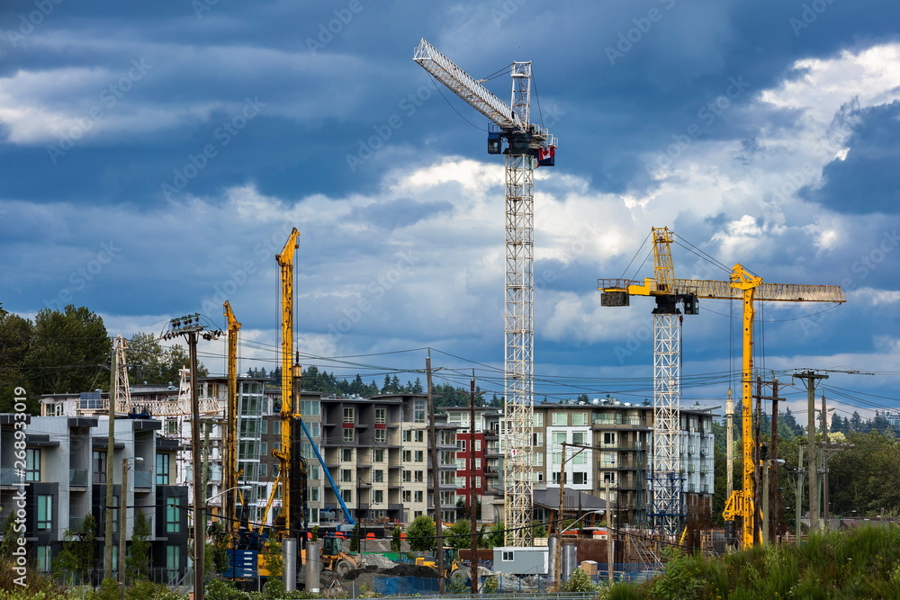 New construction of high-rise buildings in Burnaby city, industrial construction site, construction equipment, several construction cranes   on the background of finished skyscrapers and a  blue cloud