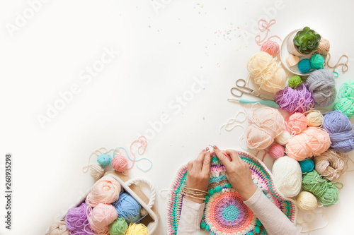Female hands knitting round mandala with color wool, on a white background, top view