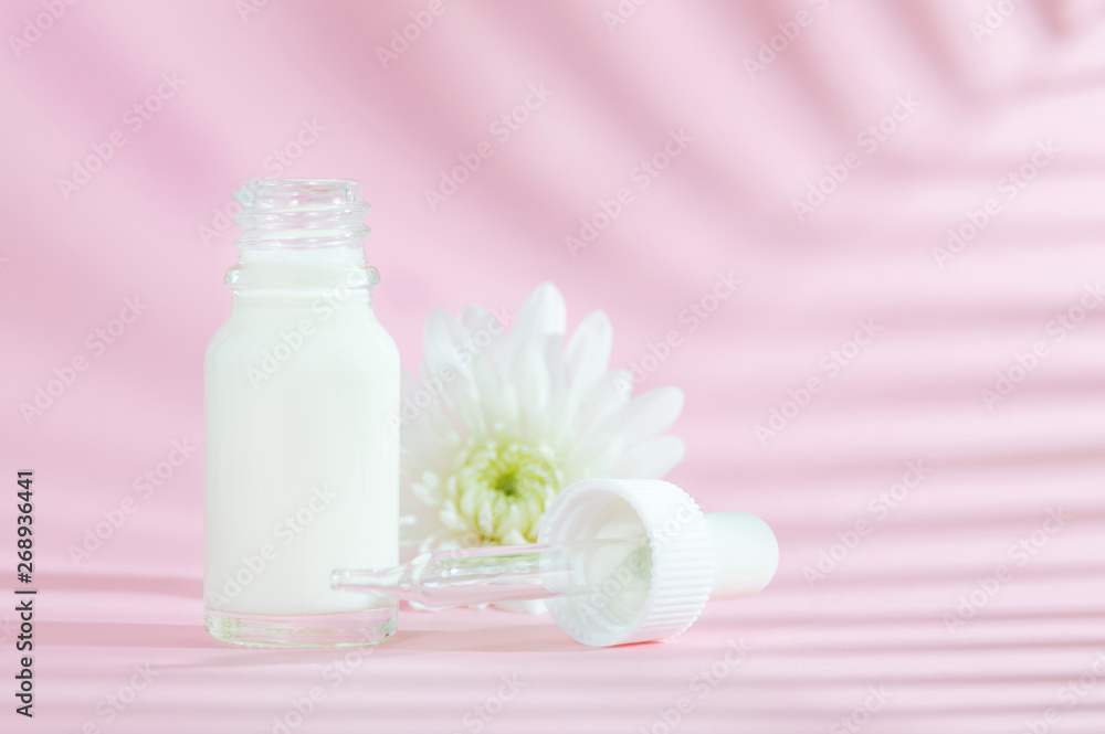 Natural cosmetics: serum with dropper and white flower on pink background with shadow. Natural cosmetics: serum with dropper and white flower on pink background with shadow.