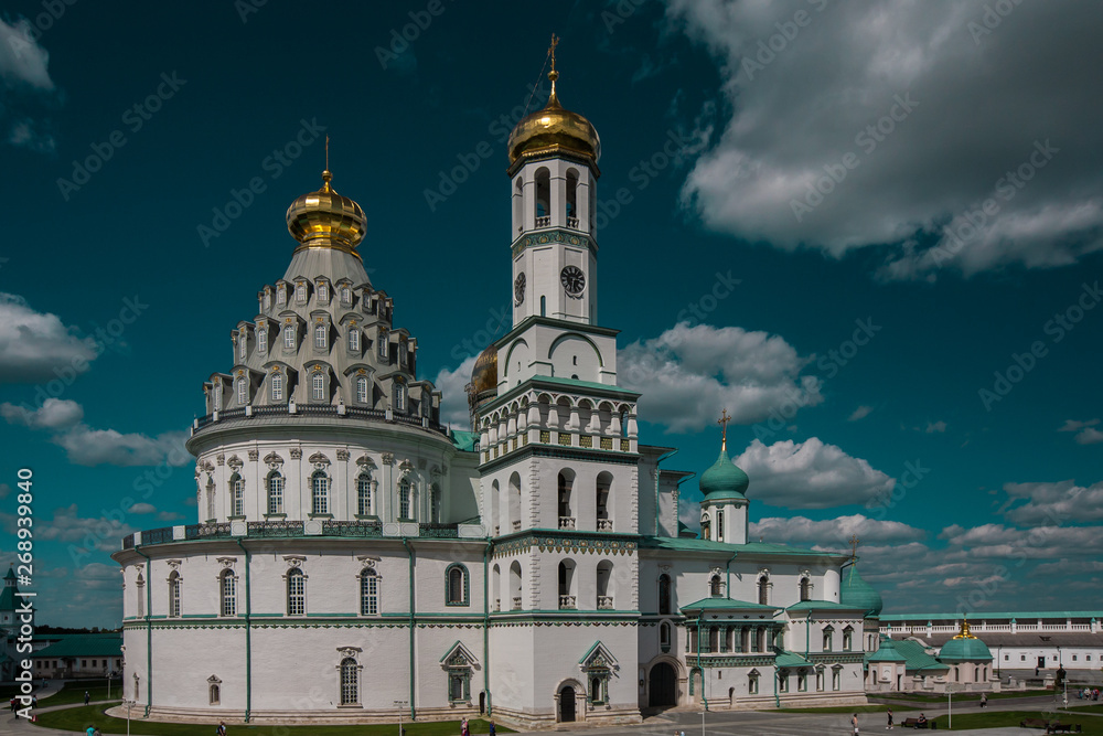 Orthodox New Jerusalem Monastery made of white stone with golden domes and turquoise rooftops against a blue sky. Famous Landmark near Moscow