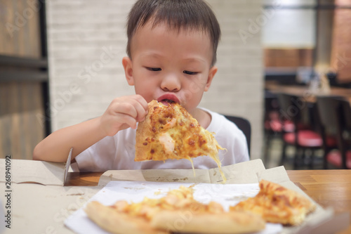 Little Asian 2 - 3 years old toddler boy child biting   eating pizza at lunch time in restaurant