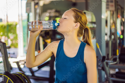 Young athletic woman drinking water in gym