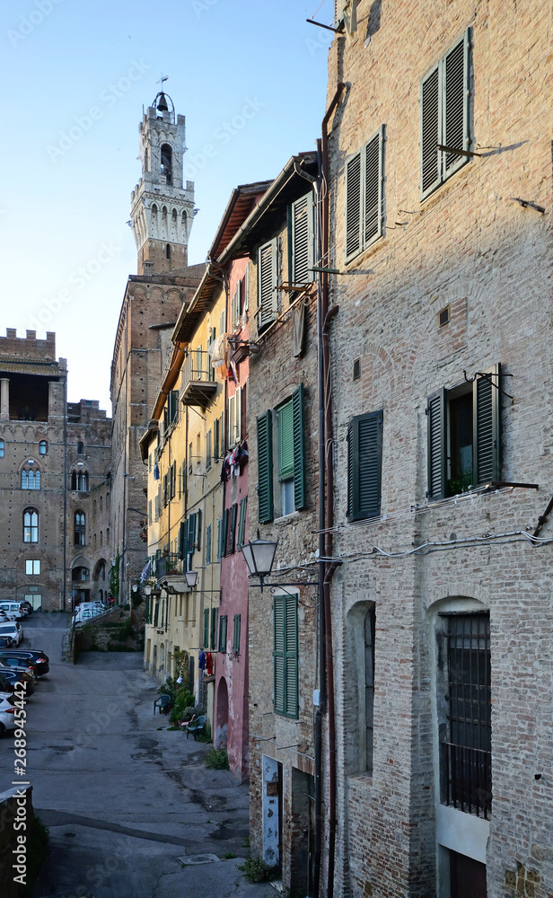 typical street view in the historic center of Siena medieval town with Torre del Mangia in the background 